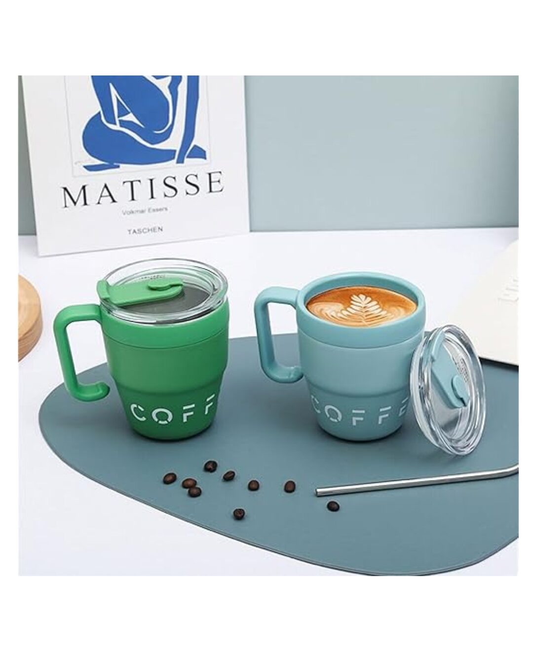 Taza térmica de acero inoxidable en verde y azul claro, con tapa antideslizante y diseño ergonómico. Incluye café con arte latte y café en grano sobre superficie azul.